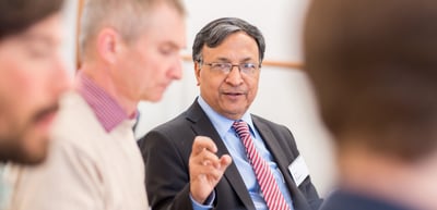 Man in a suit and tie gesturing while he talks with other participants