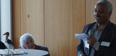 A man speaking into a microphone, a stork figure on the table