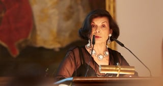 Woman with a large necklace speaking at a lectern with a microphone