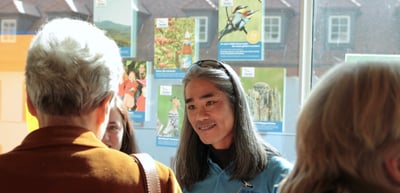 Woman with glasses on her head smiling in conversation in front of colourful posters
