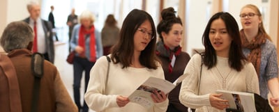 Two young women reading the convention programme in a foyer among other participants