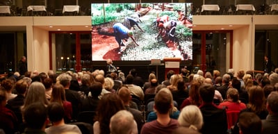 Full hall with an audience watching a projected photo of children planting trees