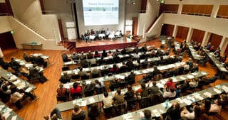 Conference hall with rows of tables seen from above, a panel seated on the stage