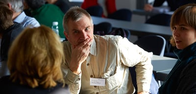 Man resting his hand on his chin while listening at a seminar table