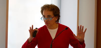 Woman in a red cardigan speaking into a microphone with raised hands