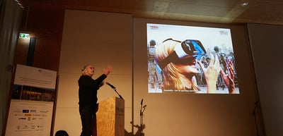 Michael Wadleigh speaking at a lectern in front of a projected image