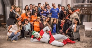 Group of young people in orange and blue T-shirts posing with a person in a superhero costume